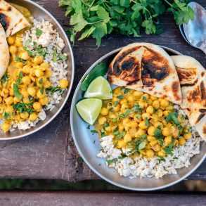 Dois pratos de curry de grão de bico de coco com arroz em uma mesa de acampamento.