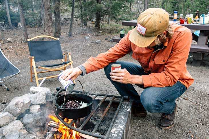 Homme cuisinant sur un feu de camp avec un four hollandais