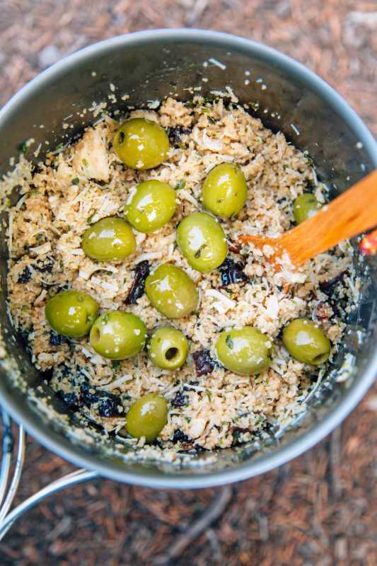 Ein Holzlöffel in einem Topf, der mit Couscous und grünen Oliven gefüllt ist