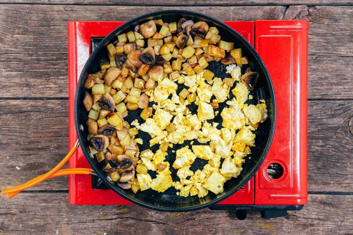 Vaření nakrájené brambory a rozdrobené tofu ve velké pánvi na míchání.