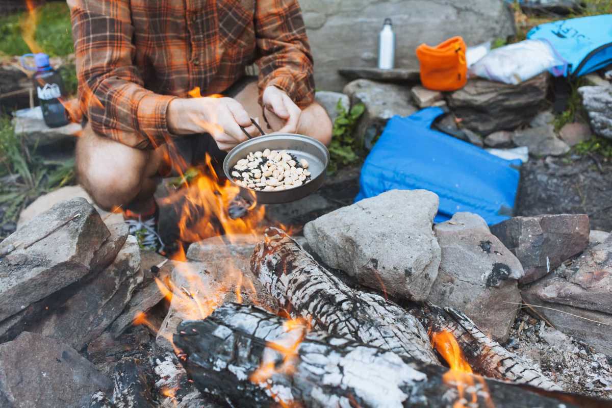 Muž vaří s malou pánví nad táborákem