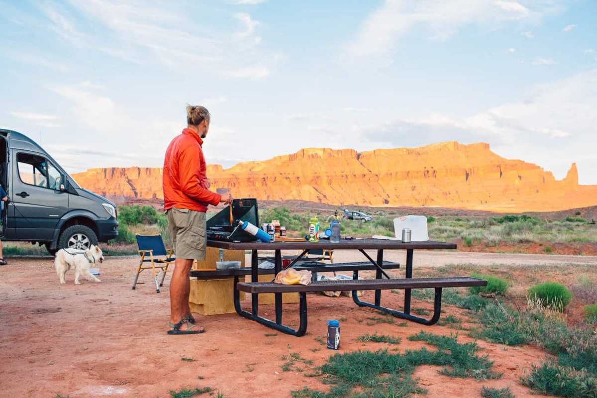 Michael kuha na štedilniku za kampiranje z rdečimi kamni v ozadju