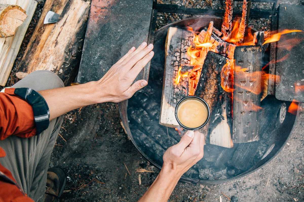 Майкъл държи чаша и топли ръцете си над лагерен огън