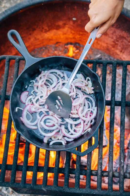 Κρεμμύδια σε φέτες σε ένα τηγάνι από χυτοσίδηρο πάνω από μια φωτιά