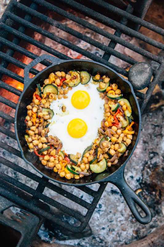 Kacang buncis dan sayuran hash dengan dua telur dalam wajan besi cor di atas api unggun