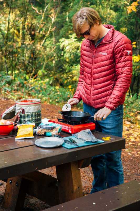 Michael parado en una mesa de camping cocinando sobre una estufa de campamento