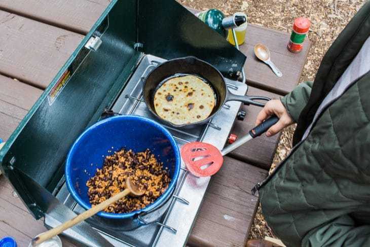 Megan kookt veganistische taco-vulling boven een kampeerfornuis