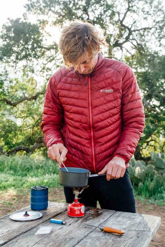 Michael debout à une table de camping en train de remuer une casserole sur un réchaud de randonnée.