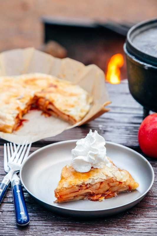 Fetta di torta di mele su un piatto con un forno olandese e un falò sullo sfondo