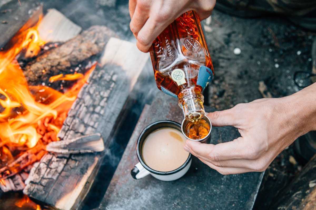 Točenje viskija v skodelico bučno začinjenega čaja s tabornim ognjem v ozadju