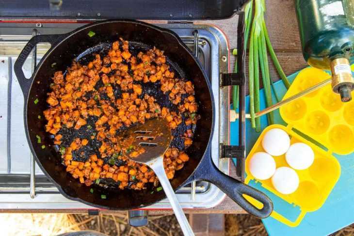 تحمير الكوريزو مع البطاطا الحلوة في مقلاة من الحديد الزهر على موقد المخيم