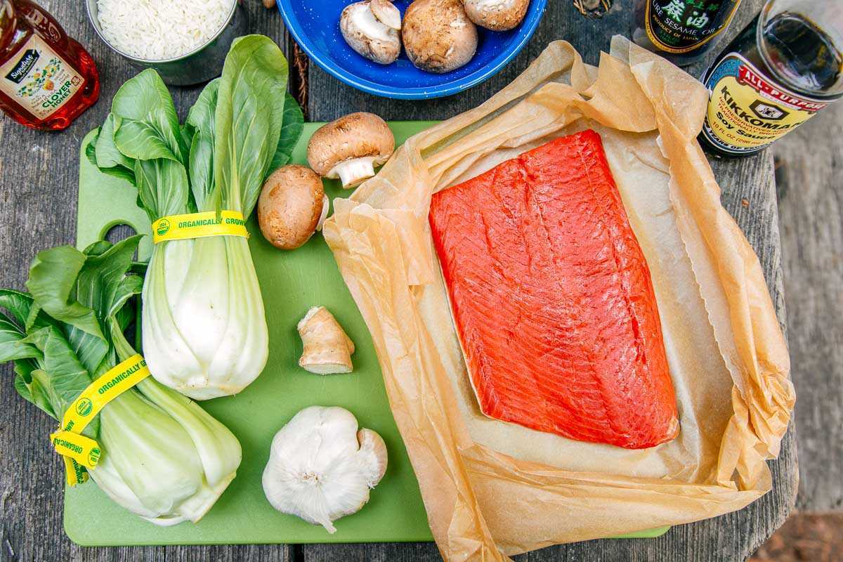 Sestavine za medeno glazirani losos na deski za rezanje: losos, bok čoj, gobe, česen in ingver.