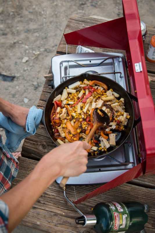 Un homme cuisinant des nouilles udon sautées dans une poêle sur un réchaud de camping
