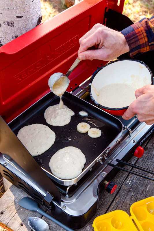 Nagdagdag si Michael ng pancake batter sa isang kawaling nasa isang camping stove