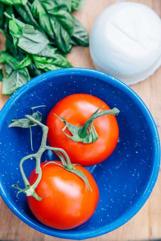 Kaks küpset tomatit kausis värske basiiliku ja mozzarella kõrvale