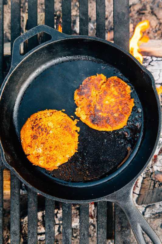 Dois hambúrgueres de batata-doce e feijão em uma frigideira de ferro fundido sobre uma fogueira