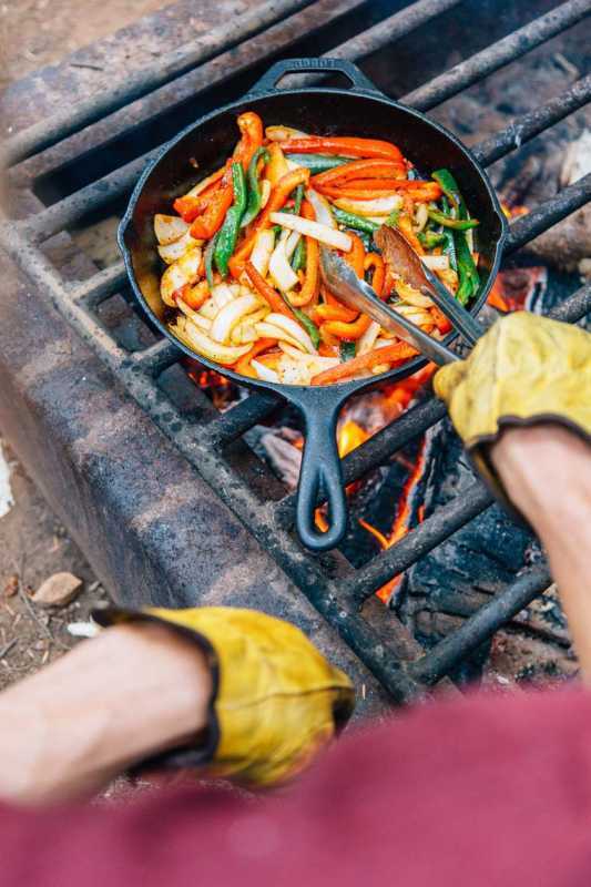 Irisan paprika dan bawang bombay dimasak dalam wajan besi cor di atas api unggun