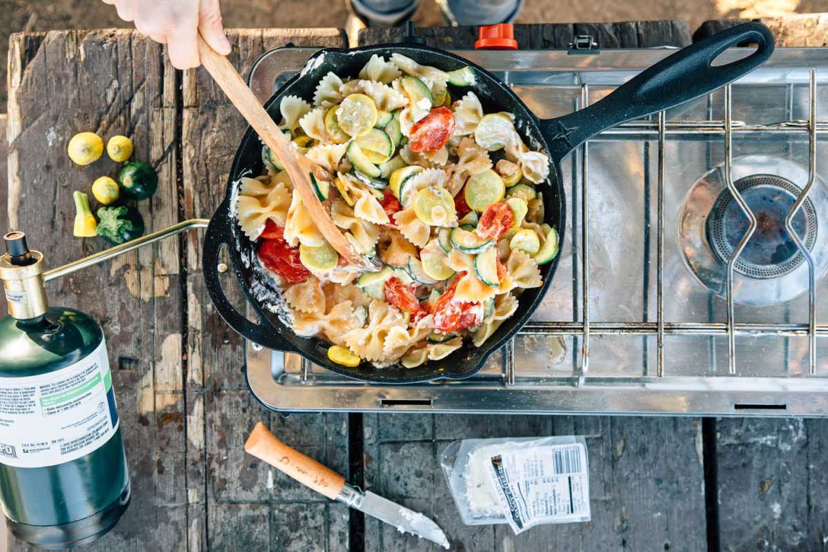 Pompoen, courgette, tomaten en pasta in een gietijzeren koekepan op een kampeerfornuis.