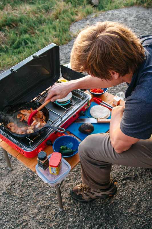 キャンプストーブの鋳鉄フライパンでエビを調理するマイケル。