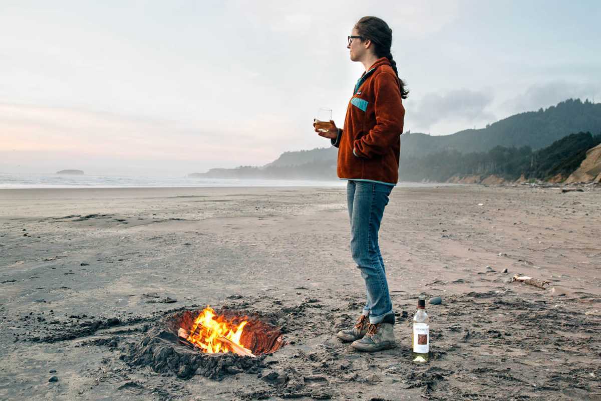 Megan stojaca pred ohňom na pláži pozdĺž pobrežia Oregonu