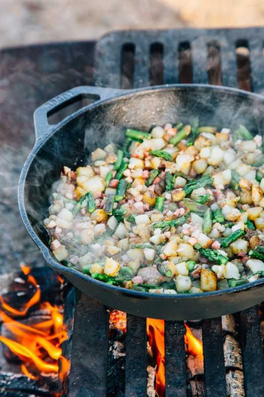 Hash kentang dan asparagus dimasak dalam wajan besi di atas api unggun