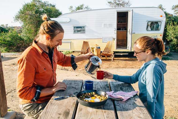 Megan y Michael se sientan en una mesa de campamento frente a un remolque antiguo. Michael le está sirviendo café a Megan.