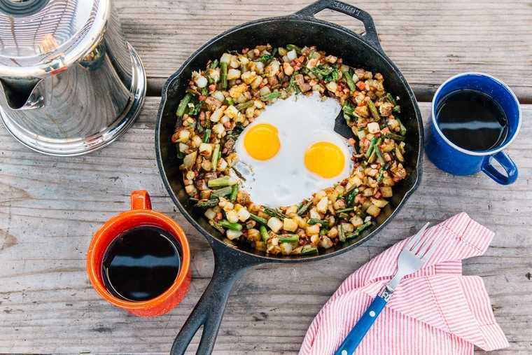 나무 캠핑 테이블 위의 주철 프라이팬에 달걀 2개를 넣은 아침 해시
