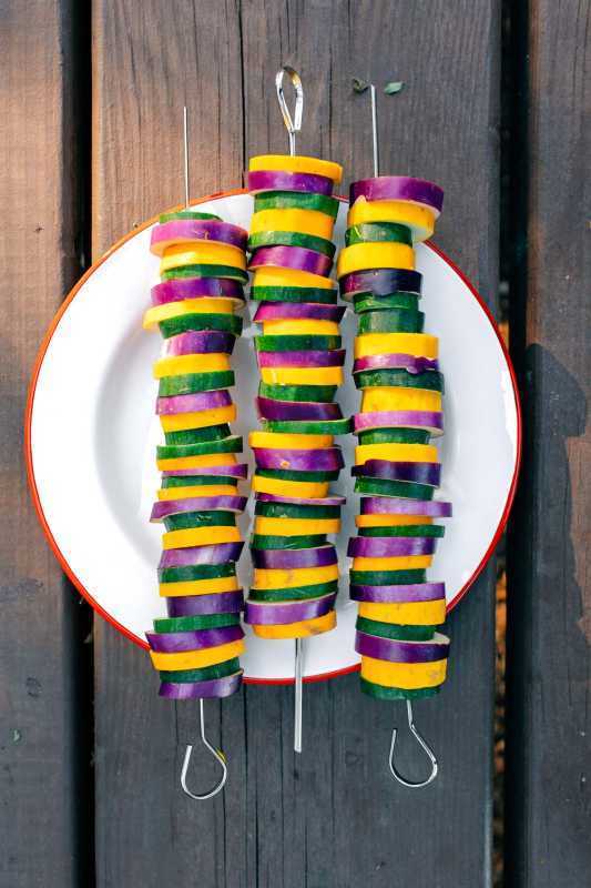 Três espetinhos de vegetais coloridos em um prato