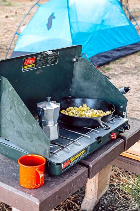 Eine gusseiserne Pfanne auf einem Campingkocher mit einem Zelt im Hintergrund