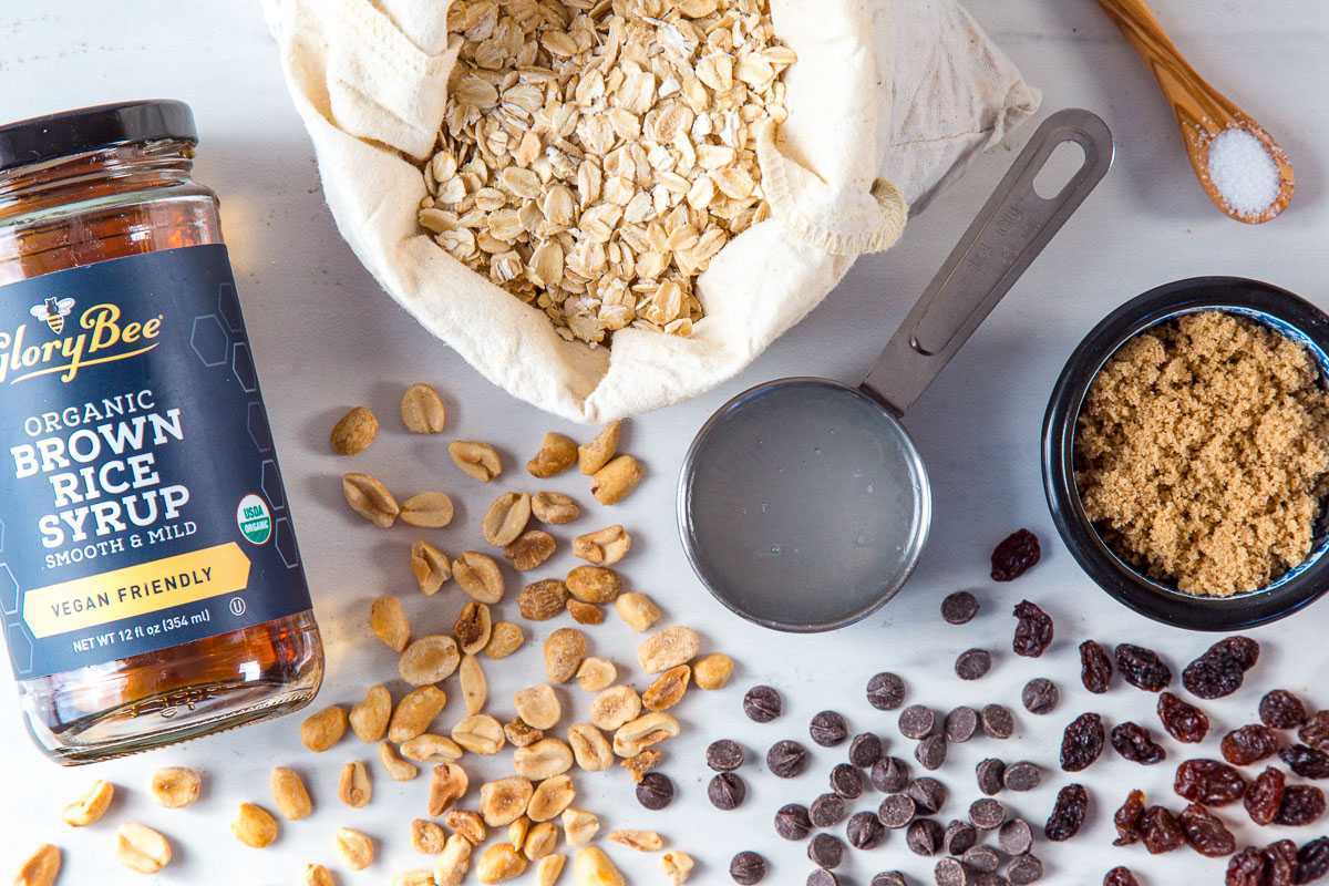 Ingrediente pentru bara granola: ovăz rulat, sirop de orez brun, ulei de cocos, zahăr brun, arahide, chipsuri de ciocolată și stafide