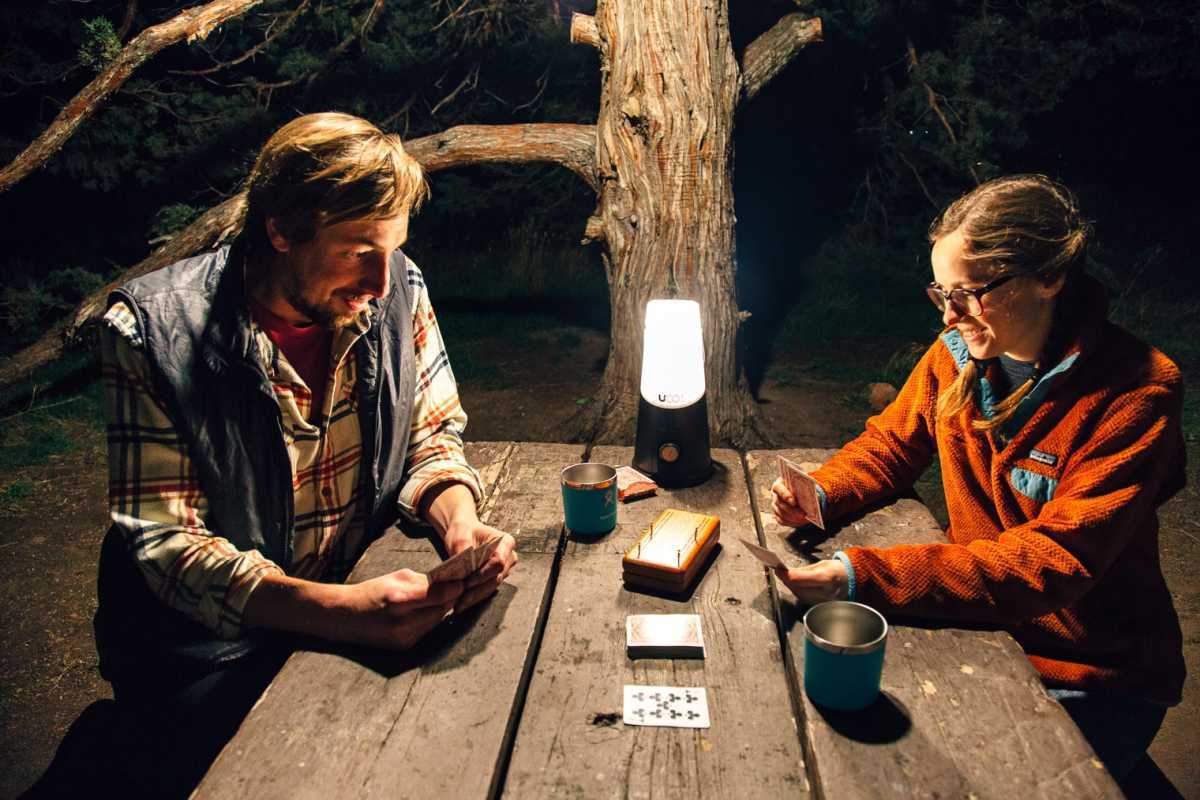 Megana un Maikls spēlē kārtis pie laternas apgaismota galda
