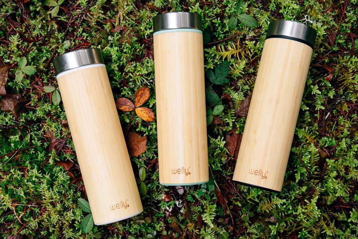 Три бамбуковые бутылки с водой на мшистой поверхности.